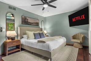 A bedroom with a bed, nightstands, a lamp, a chair, a ceiling fan, a wall-mounted TV, and a painting. - Heated Pool - Hot Tub - Sauna - Game Room - Pets (Sun Prairie)