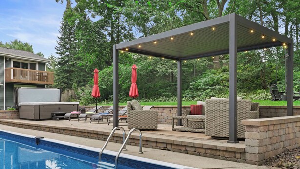 A backyard with a swimming pool, outdoor furniture, and a covered seating area.