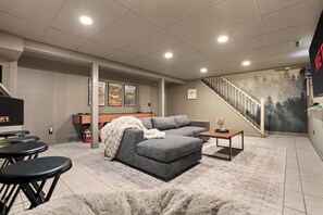 A modern living room with a sectional sofa, a coffee table, and a staircase leading to a balcony. - Heated Pool - Hot Tub - Sauna - Game Room - Pets (Sun Prairie)