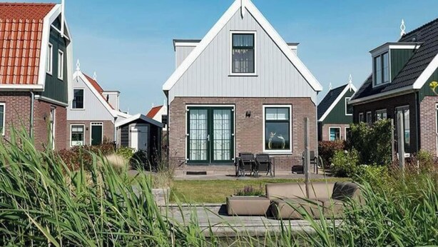Et moderne hus med en stor hoveddør, en lille terrasse med udendørs møbler og en velplejet have.