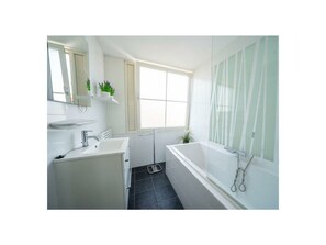 A bathroom with a white sink, mirror, and bathtub. There is a window with a view of the outside. - Holiday Home in Uitdam With Sauna (Uitdam)