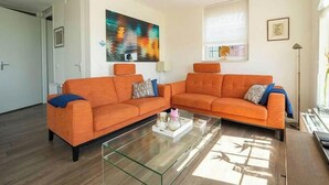 En stue med to orange sofaer, et sofabord i glas og et billede på væggen.