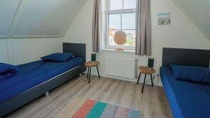 Et værelse med to senge, et vindue med gardiner, en radiator og en lille måtte.