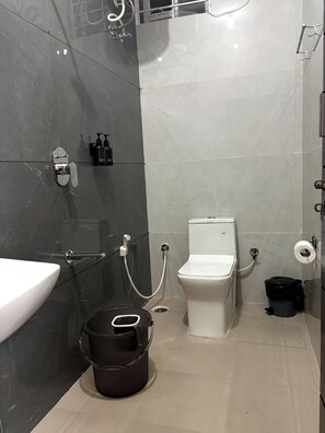 A bathroom with a white sink, toilet, and bidet, a black bucket, and a shower area. - Luxury Stay 20 mins away from Airport! (Bengaluru)