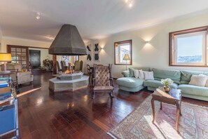 A spacious living room with a fireplace, a green sofa, and a wooden coffee table. - Waterfront Villa by Douro w/ BBQ & River Views (Avintes)