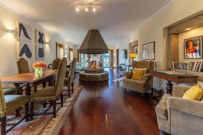 A spacious living room with a dining area, a fireplace, and a large window offering a view. - Waterfront Villa by Douro w/ BBQ & River Views (Avintes)