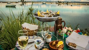 Ein Tisch, gedeckt mit Austern, Weingläsern und einer Tasse, an einem ruhigen See mit Booten im Hintergrund.