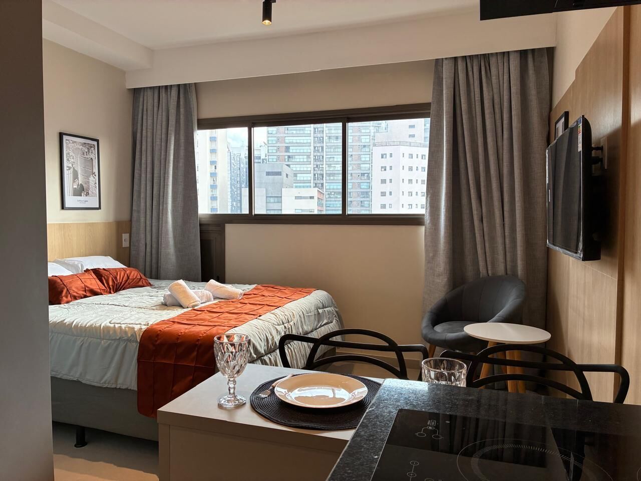 A hotel room with a bed, a desk with a chair, a television, and a window with curtains.