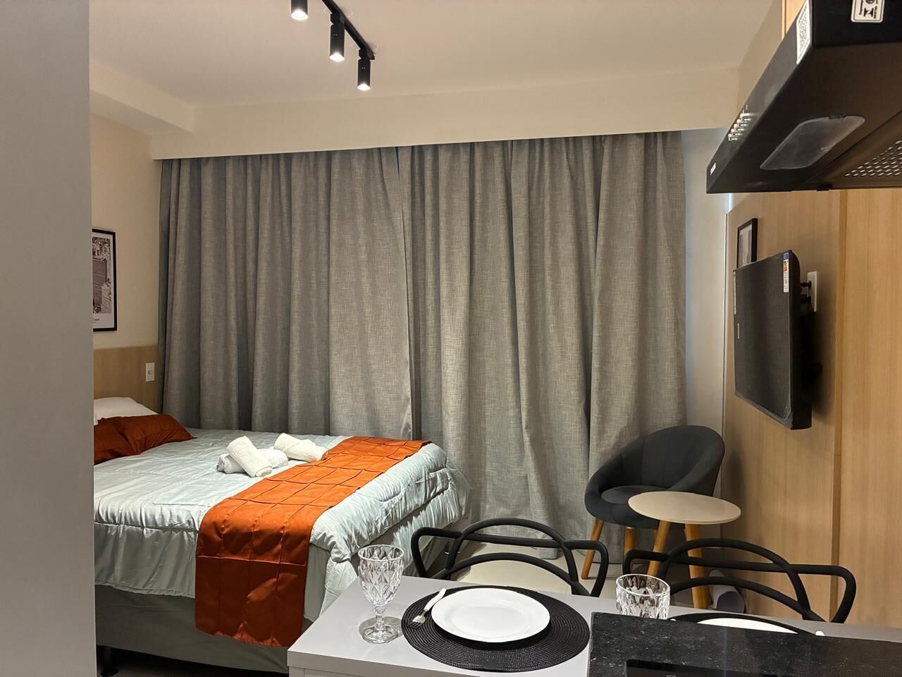 Ein Hotelzimmer mit Bett, Schreibtisch mit Stuhl, Fernseher und einem Fenster mit Vorhängen.