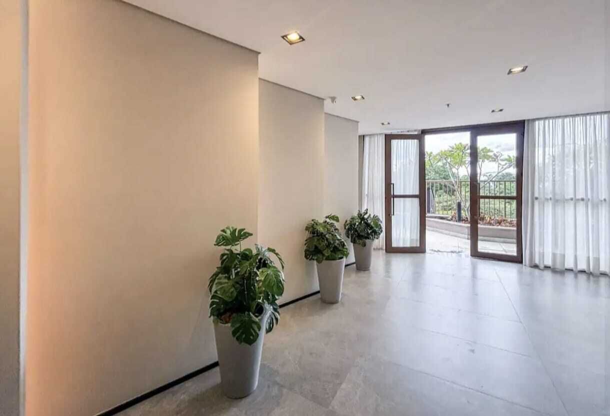 A spacious interior with a modern design, featuring a large open area with potted plants and a view through glass doors.