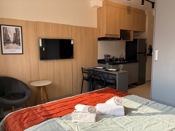 A hotel room with a bed, a TV, a small dining table with chairs, and a kitchenette.