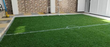 A room with a green artificial turf floor, a white door, and a tiled wall with a brick pattern.
