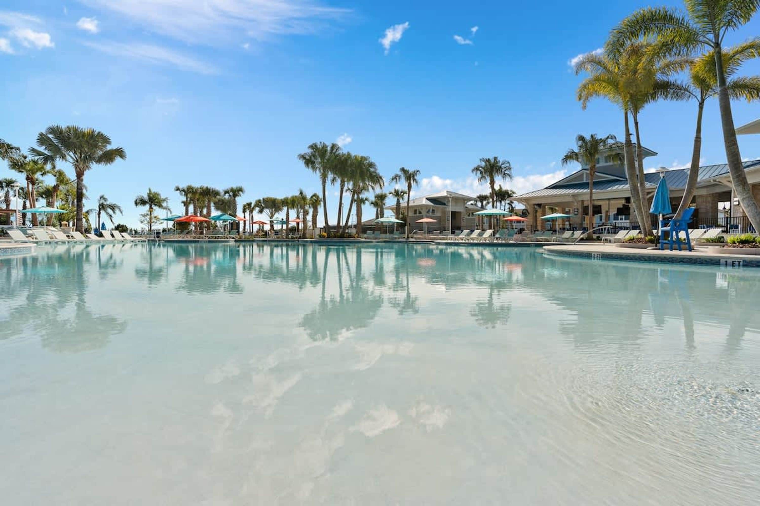 Un área de piscina con sillones de descanso, sombrillas y palmeras.