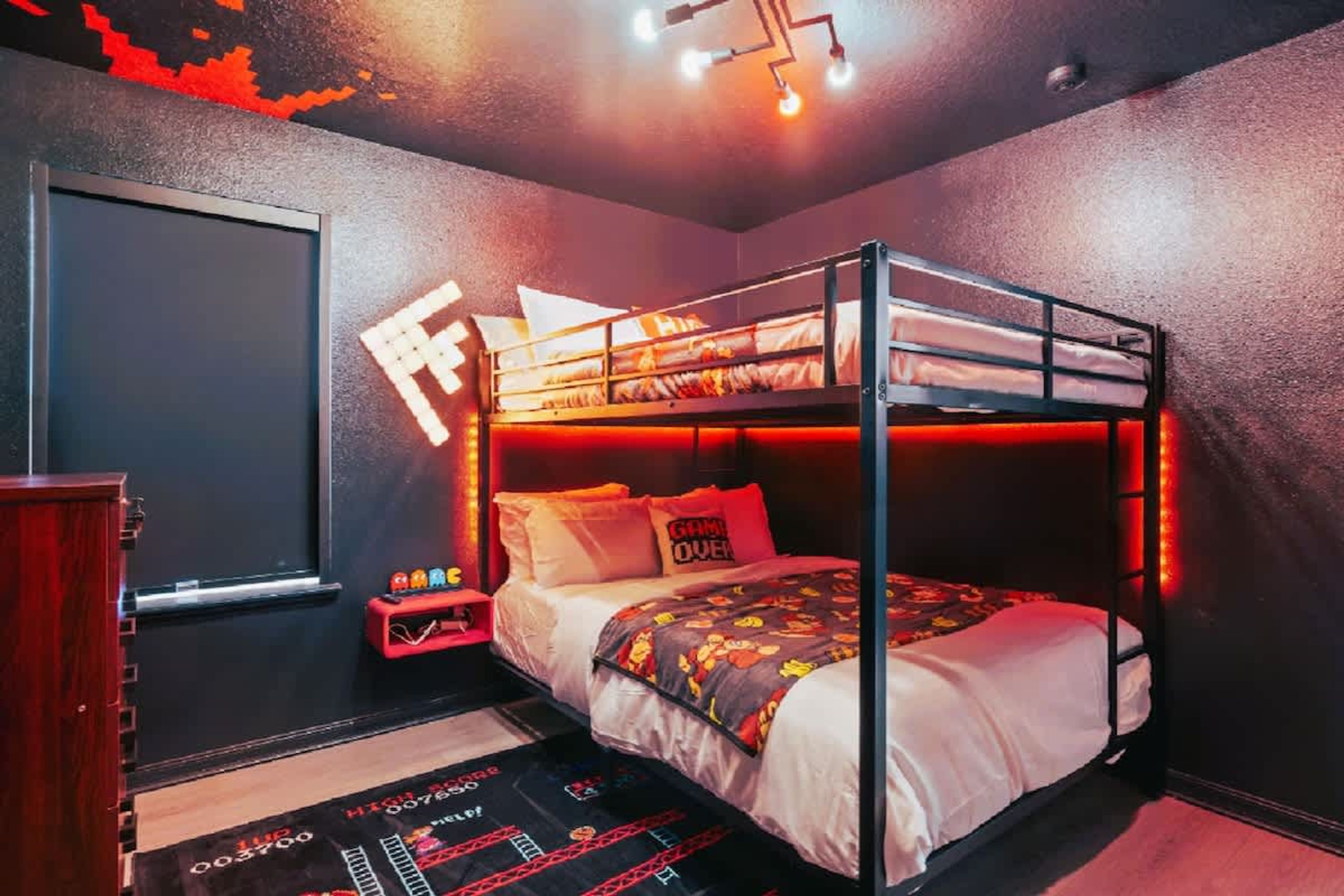 Een slaapkamer met stapelbedden, een rode en witte kleurenschema, een klein bureau met stoel en een wandplank.