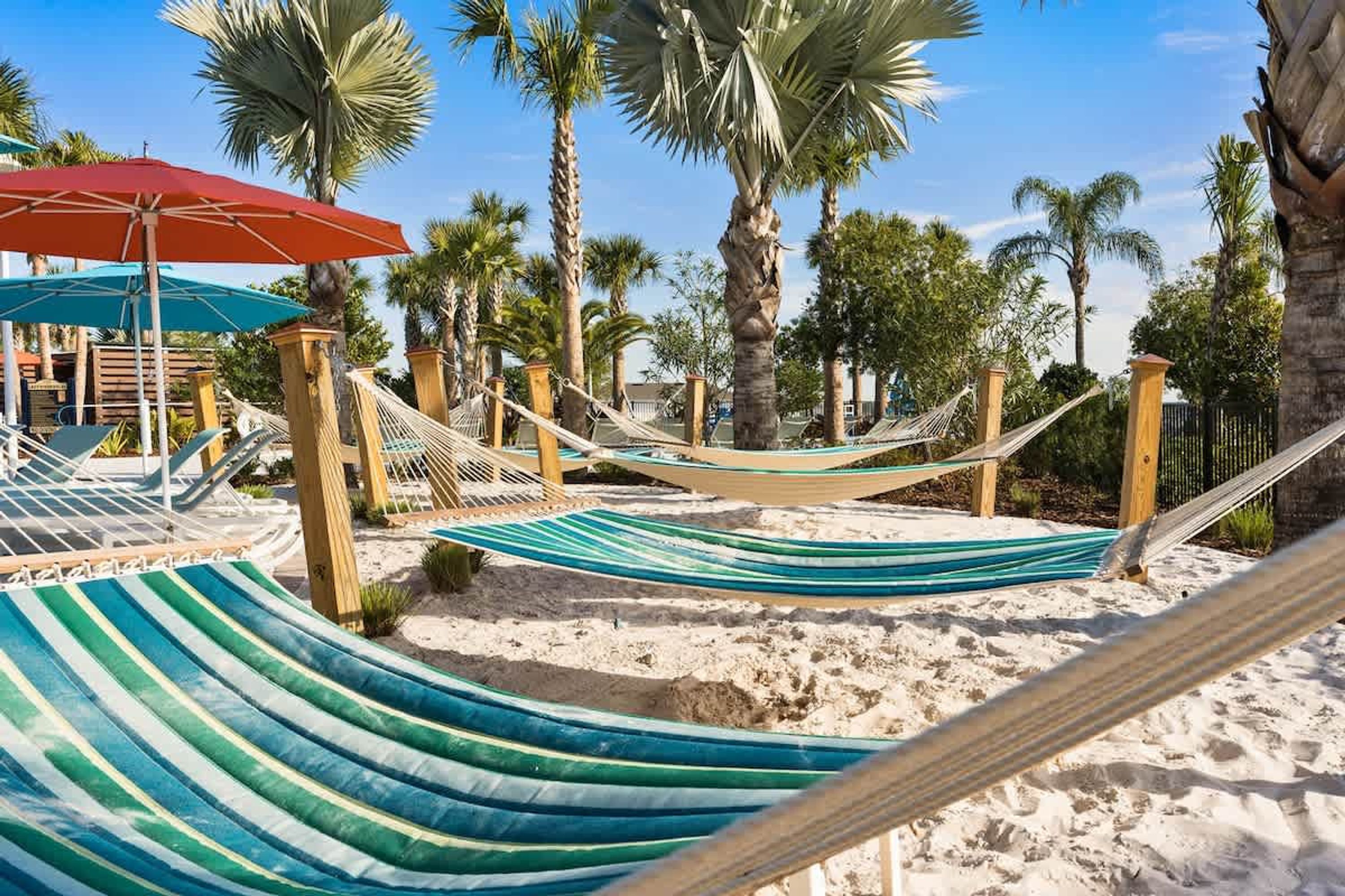 A hammock set up on a sandy beach with palm trees in the background.