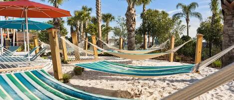 A hammock set up on a sandy beach with palm trees in the background.