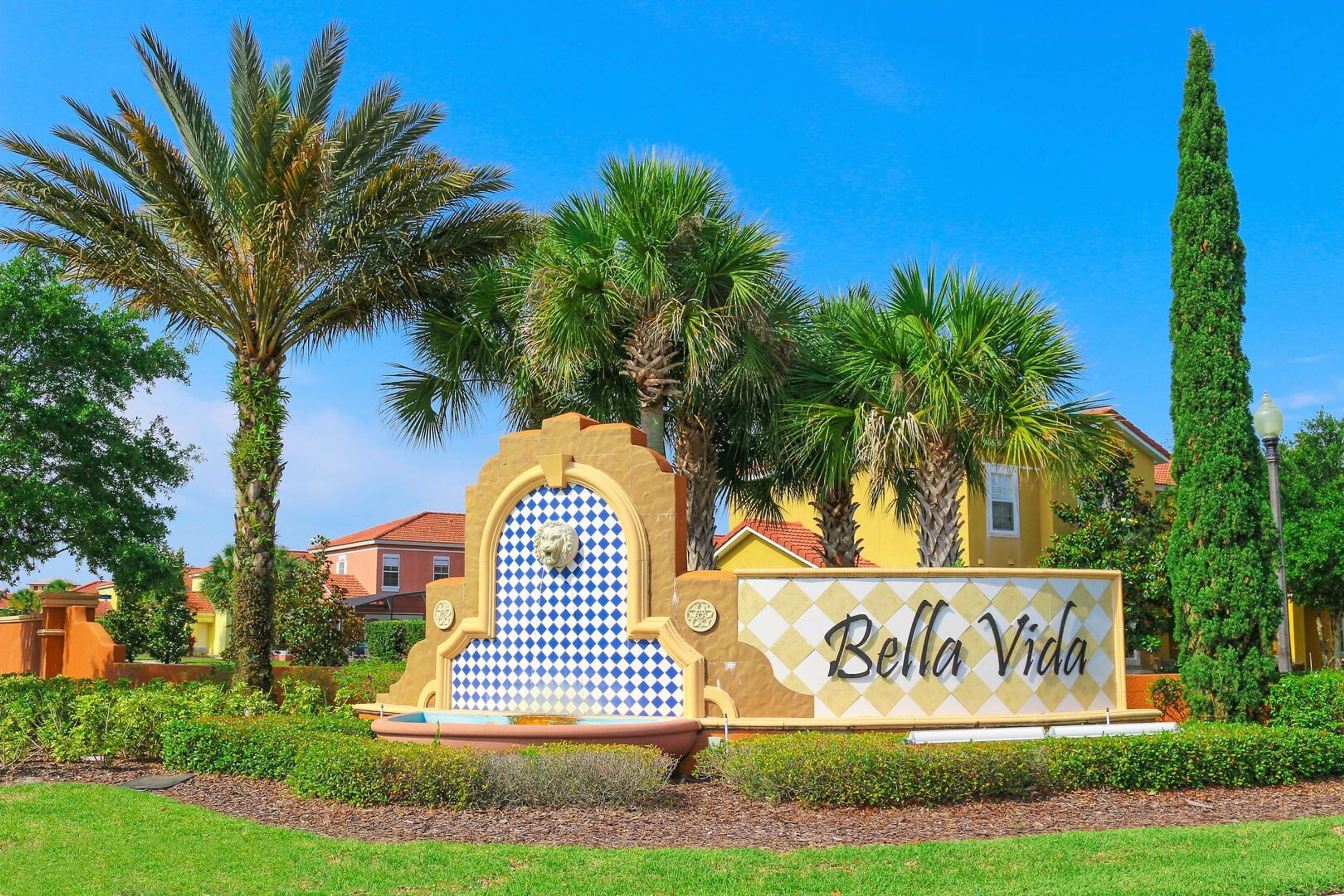 A sign with 'Bella Vida' written on it, surrounded by palm trees and a clear blue sky.