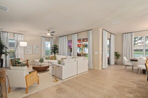 A spacious living room with a white sofa, a round coffee table, and a dining area with a table and chairs. - Disney Themed Resort Home With Lake View (Kissimmee)