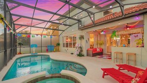 An indoor swimming pool with a glass ceiling, red lounge chairs, and a colorful interior. - Disney Themed Resort Home With Lake View (Kissimmee)