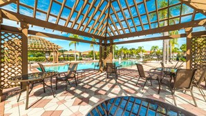 A covered outdoor area with a pool, chairs, and a pergola structure. - Disney Themed Resort Home With Lake View (Kissimmee)