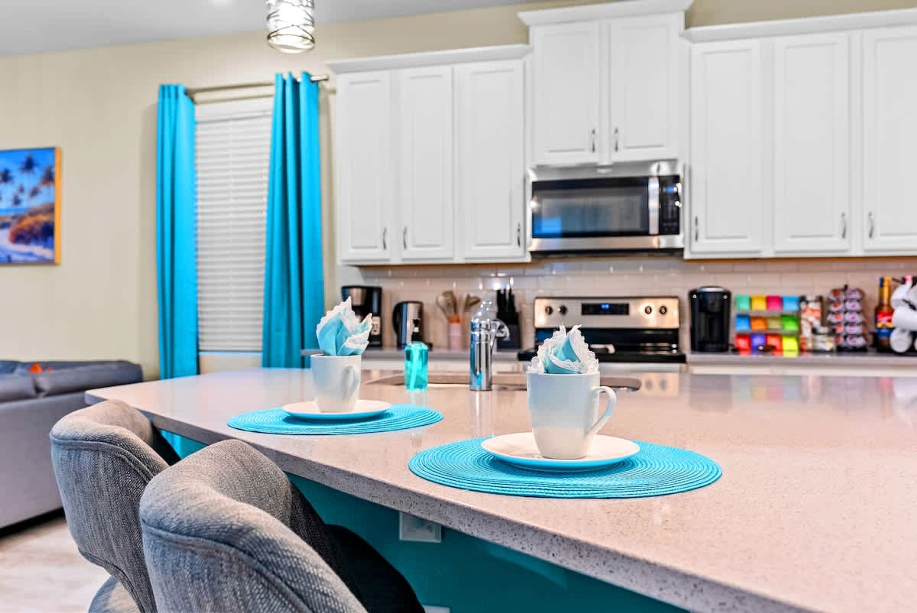 A kitchen with white cabinets, a microwave, and a coffee station with two cups and a blue placemat.