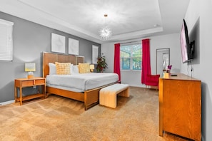 A bedroom with a bed, bedside tables, a desk, a chair, a TV, and a window with curtains. - Resort Home With Pool Spa Game Room Near Disney (Kissimmee)