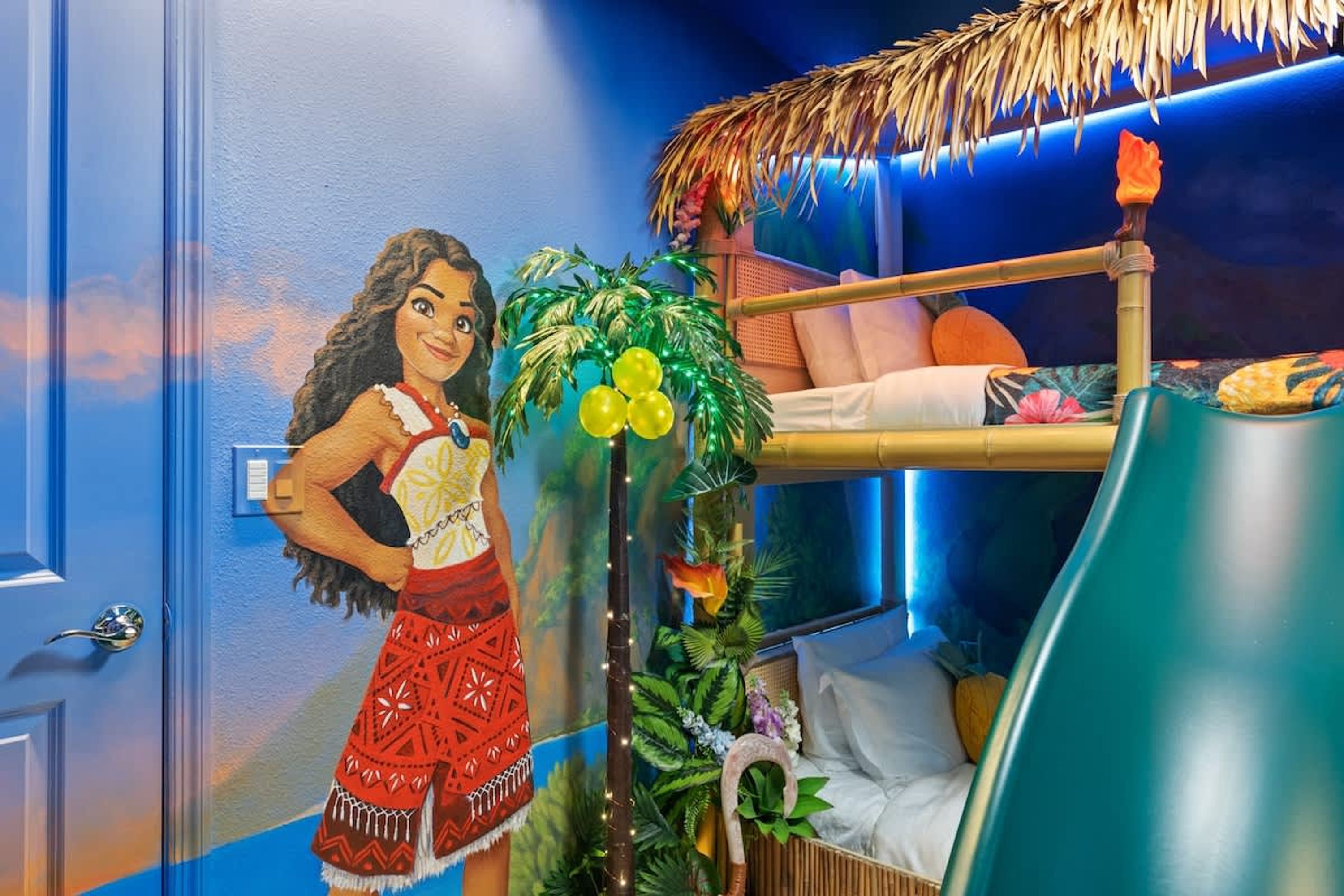 Et værelse med køjeseng, et muralmaleri, en plante og en tiki-fakkel.