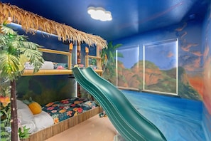 Une chambre avec un lit superposé, un toboggan et une fresque représentant un paysage tropical.