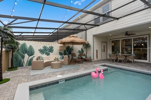 Un espace piscine agrémenté d’un parasol en chaume, de chaises longues et d’un flotteur en forme de flamant rose.