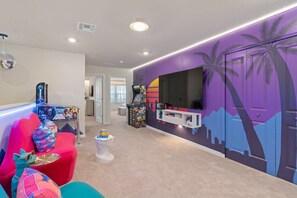 Ein modernes Wohnzimmer mit einem farbenfrohen Sofa, einer Spielkonsole und einem Wandbild.