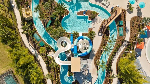Vista aérea de un complejo turístico con una piscina grande, toboganes acuáticos y palmeras.
