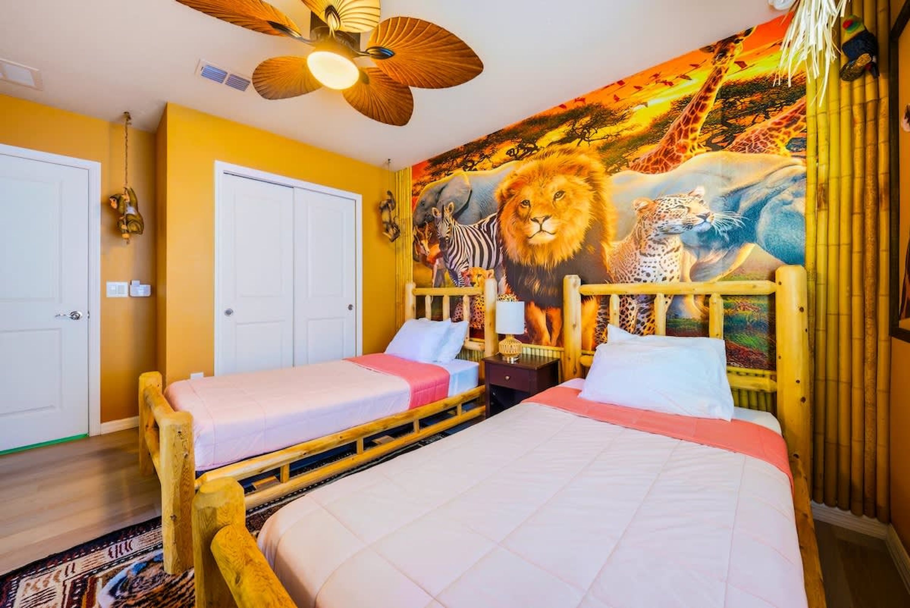 A room with two wooden beds, a ceiling fan, and a mural of African wildlife on the wall.