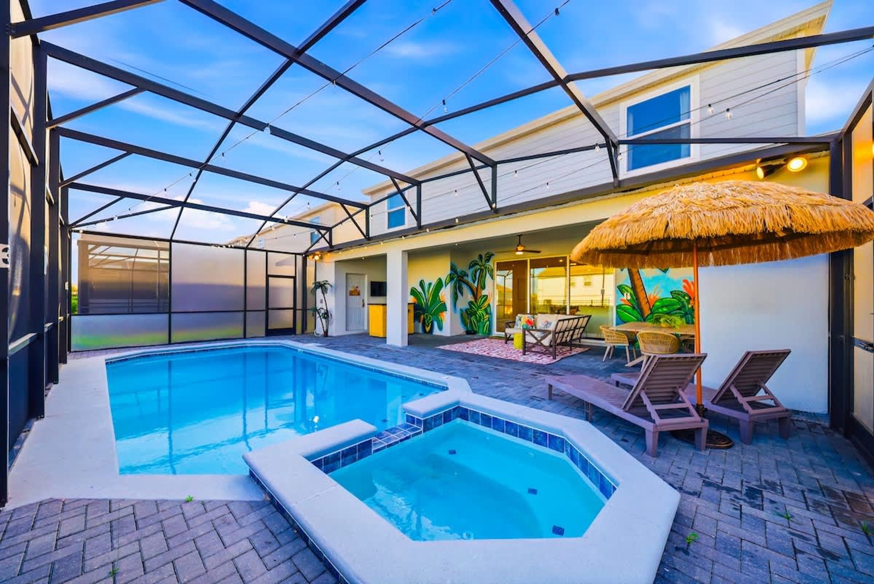 Une piscine avec un jacuzzi, des chaises longues et un parasol en chaume.