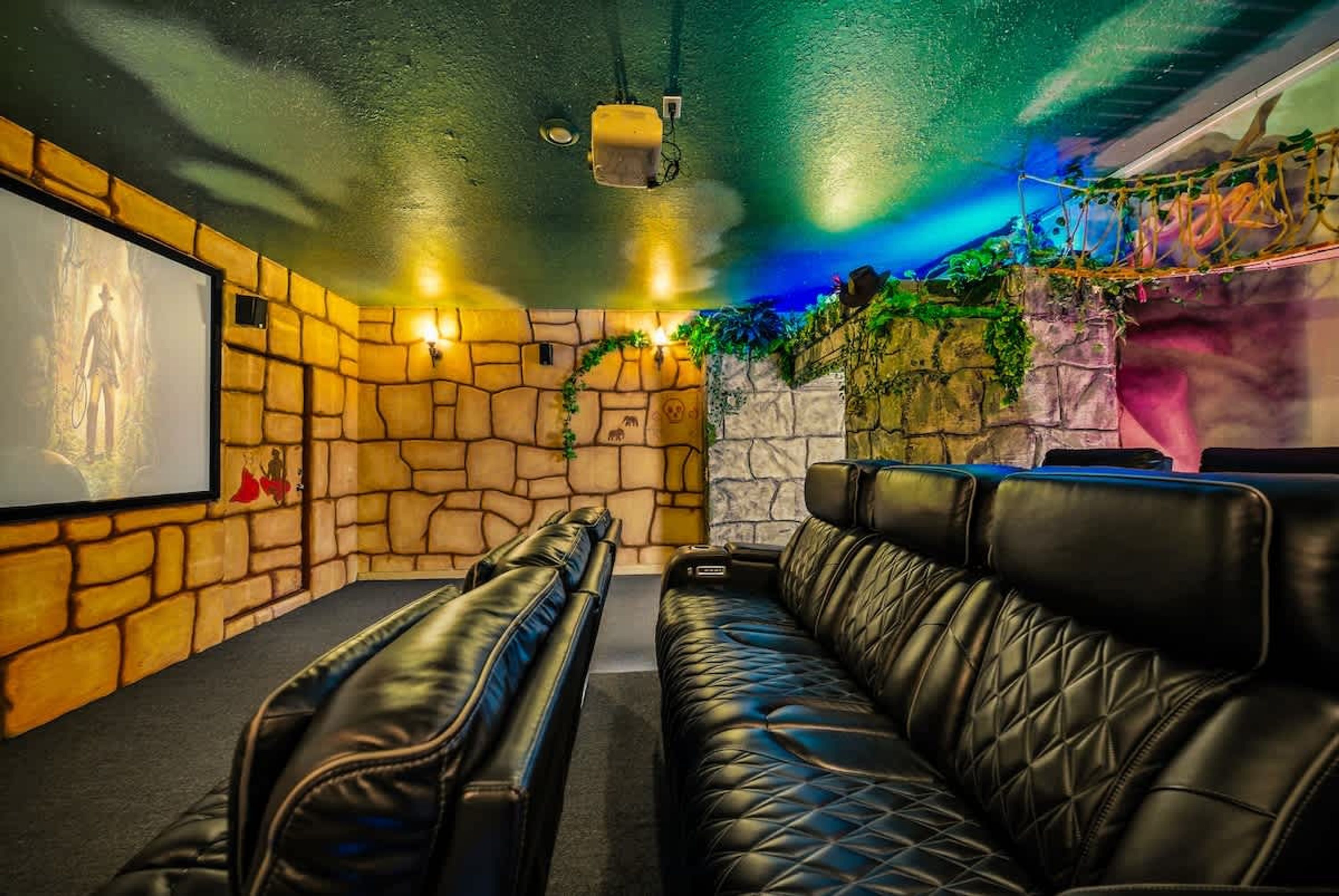 A room with stone walls, a black leather couch, and a projector screen.