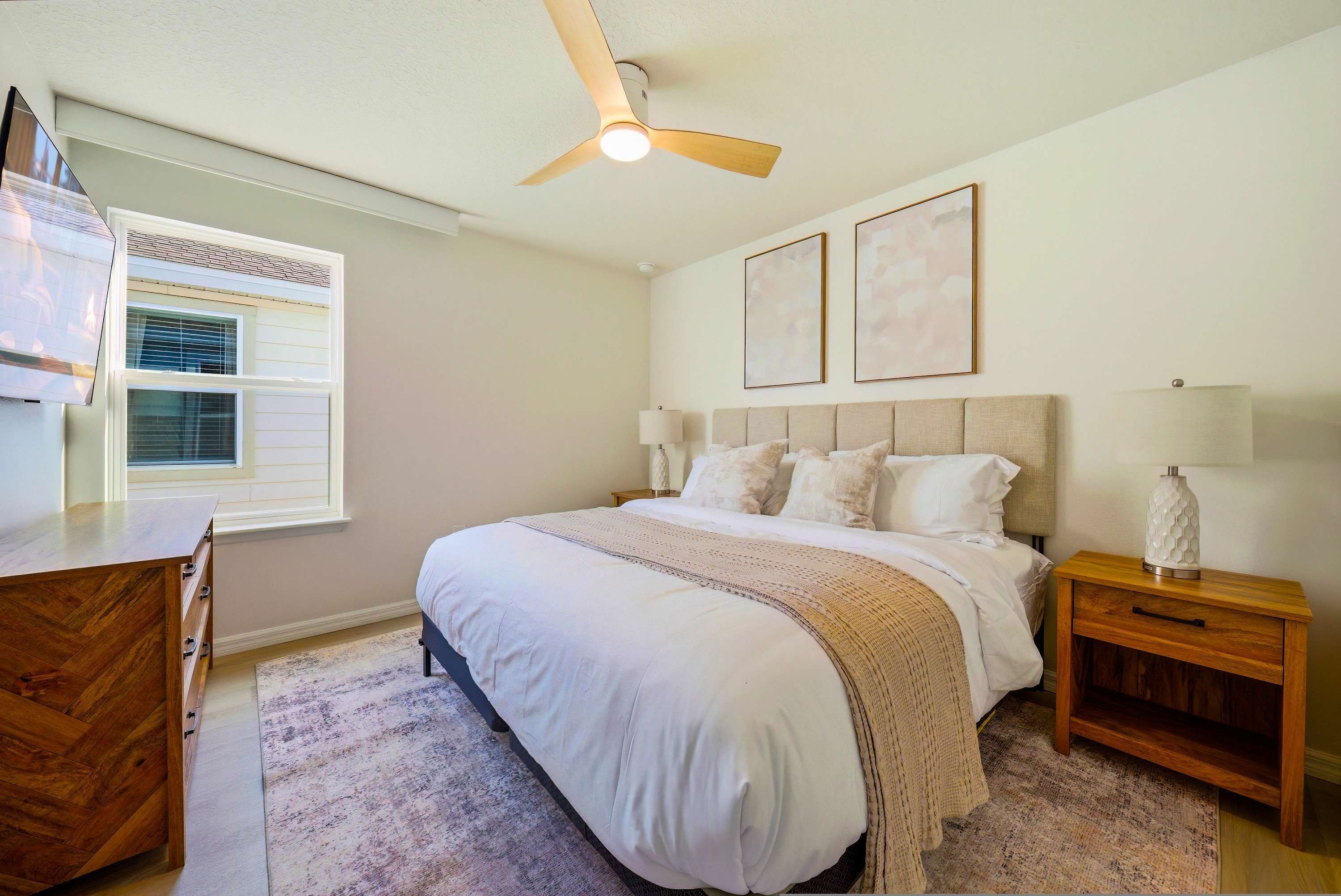 A bedroom with a bed, bedside tables, a ceiling fan, a desk, and a window with blinds.