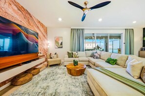 A modern living room with a flat-screen TV, a ceiling fan, a sectional sofa, and a large window. - Windsor Resort Private Pool Theater Game Room (Davenport)