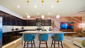 Una cocina moderna con armarios oscuros, una isla central con taburetes y un televisor de pantalla plana montado en la pared.