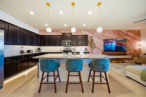 A modern kitchen with dark cabinets, a central island with bar stools, and a flat-screen TV mounted on the wall. - Windsor Resort Private Pool Theater Game Room (Davenport)