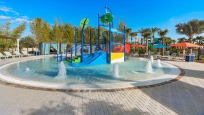 Un área de juegos acuáticos con piscina circular, una estructura para escalar y sillas de descanso alrededor de la piscina.