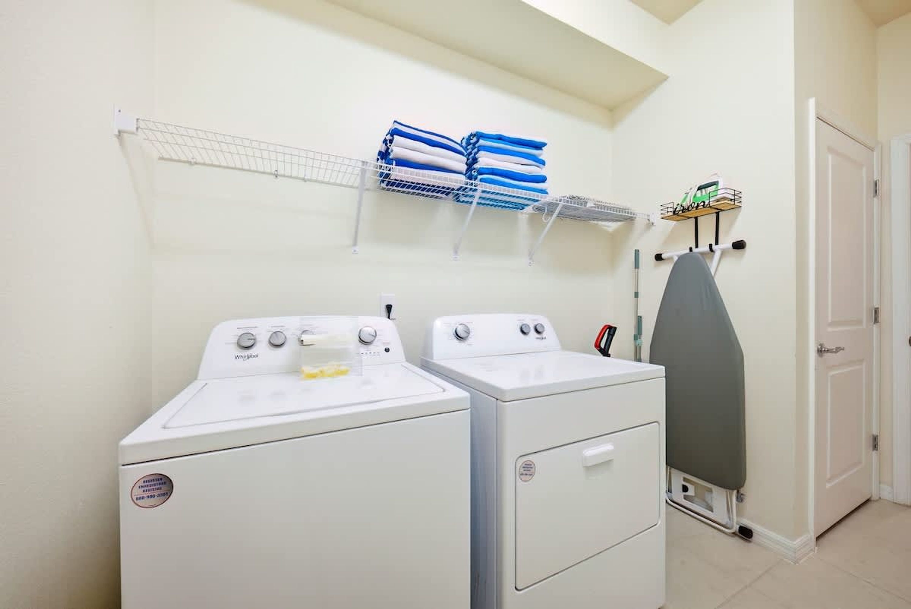 A laundry area with two white washing machines, a drying rack with folded towels, and an ironing board.
