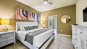 A bedroom with a bed, bedside tables, a dresser, a ceiling fan, a mirror, and abstract wall art. - Resort Home Private Pool and Spa Outdoor Theater (Kissimmee)