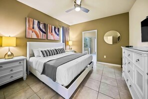 A bedroom with a bed, bedside tables, a dresser, a ceiling fan, a mirror, and abstract wall art. - Resort Home Private Pool and Spa Outdoor Theater (Kissimmee)