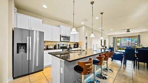 A modern kitchen with a central island, stainless steel appliances, and bar stools. - Resort Home Private Pool and Spa Outdoor Theater (Kissimmee)
