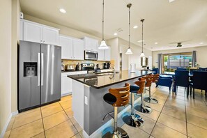 A modern kitchen with a central island, stainless steel appliances, and bar stools. - Resort Home Private Pool and Spa Outdoor Theater (Kissimmee)