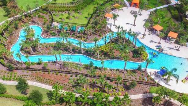 Une grande piscine sinueuse, dotée de plusieurs couloirs, entourée de palmiers et bordée d’une zone sablonneuse avec des chaises longues.