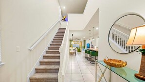 Un escalier menant à un espace repas avec une table et des chaises en verre, une suspension décorative et une lampe posée sur une étagère en verre.