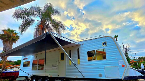 A blue RV with a covered porch, a ladder, and a palm tree in the background. - Peaceful 1-bedroom recreational vehicle with AC in Spring Valley (Spring Valley)
