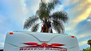 A white RV with 'Weekend Warrior' branding, a water pump, and a palm tree in the background. - Peaceful 1-bedroom recreational vehicle with AC in Spring Valley (Spring Valley)