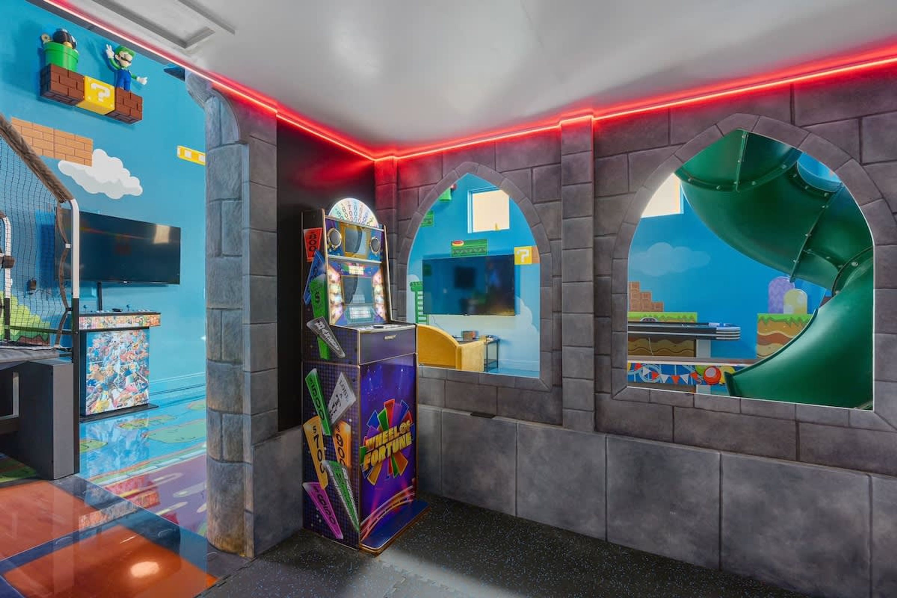 A room with a Nintendo-themed wall, a wheel of fortune game, and a window with a view of a green slide.