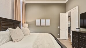 Ein Schlafzimmer mit einem großen Bett, einem Schminktisch, einem Fernseher und einer Tür zu einem anderen Raum.